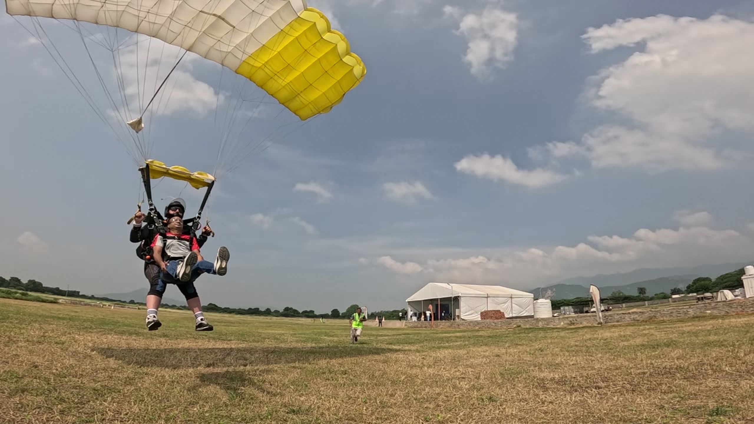 Tandem pair landing beneath a yellow parachute at the Mount Abu dropzone